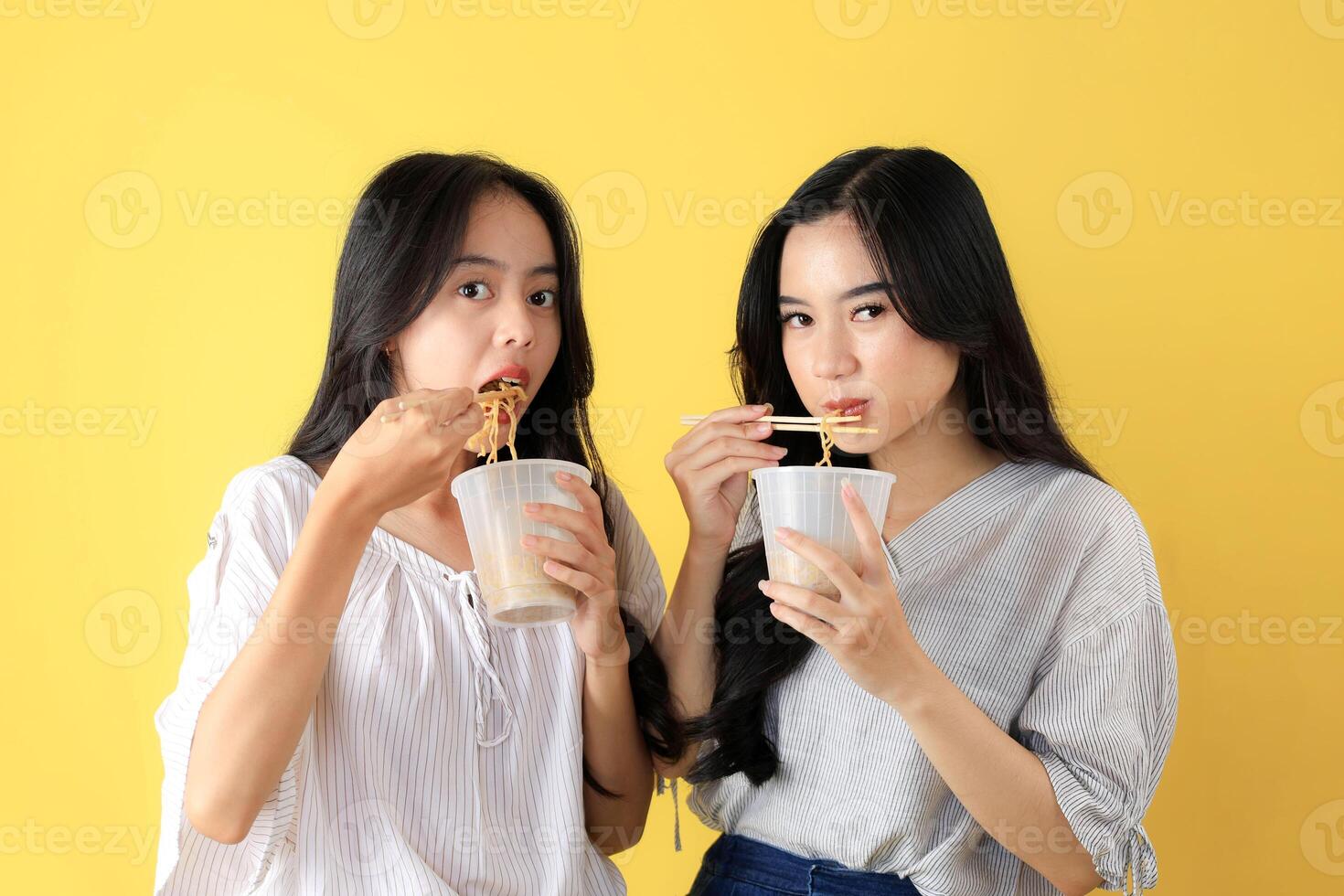 Two Young Asian Girl Holding A Cup of Instant Noodle, Isolated on Yellow Background. photo