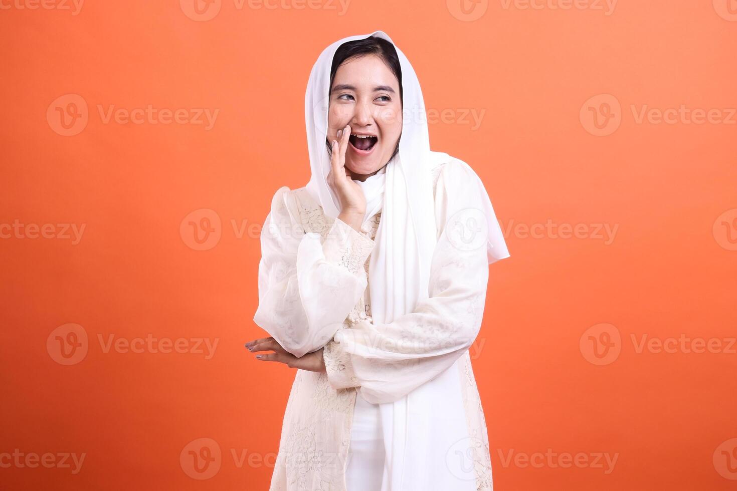 Excited young woman in white hijab, whispering a secret, radiate photo