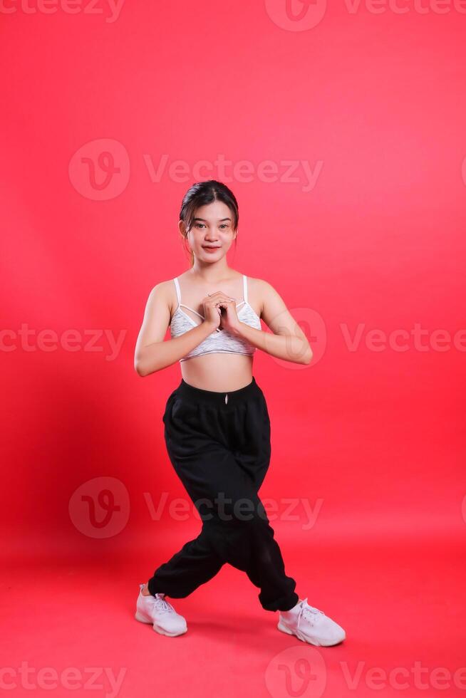 A woman dressed in a sport outfit with a white top and black pants posing, hands clasped in front of her, isolated on a red background. photo