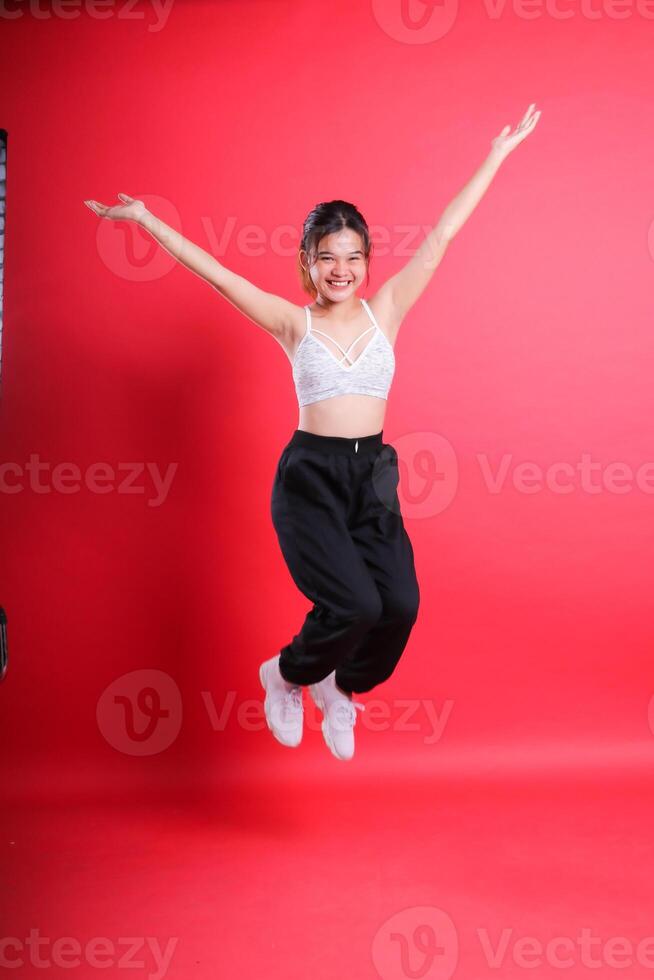 A person with a white top and black pants, jumping with arms outstretched. isolated on a red background photo