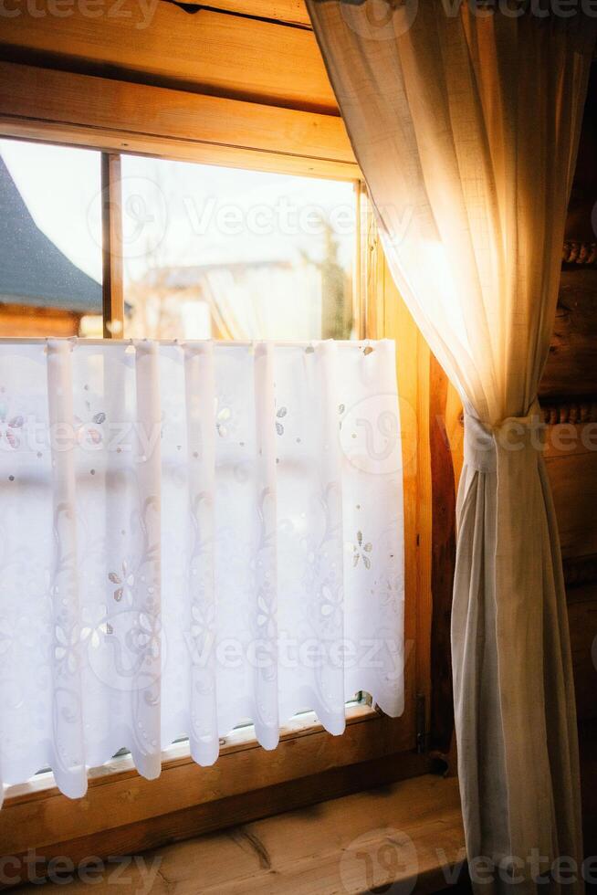 Sunlight streaming through sheer white curtains in cozy wooden cabin creates warm and inviting atmosphere, enhancing serene interior with natural light and rustic charm. Soft sunlight, wooden interior photo