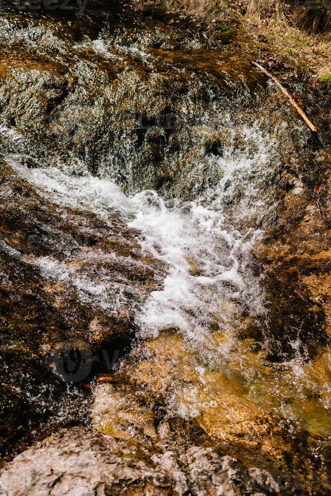 Crystal clear water flows over moss covered rocks, creating mesmerizing cascade in pristine natural setting, showcasing beauty and tranquility of untouched wilderness. Water cascading over moss rocks photo