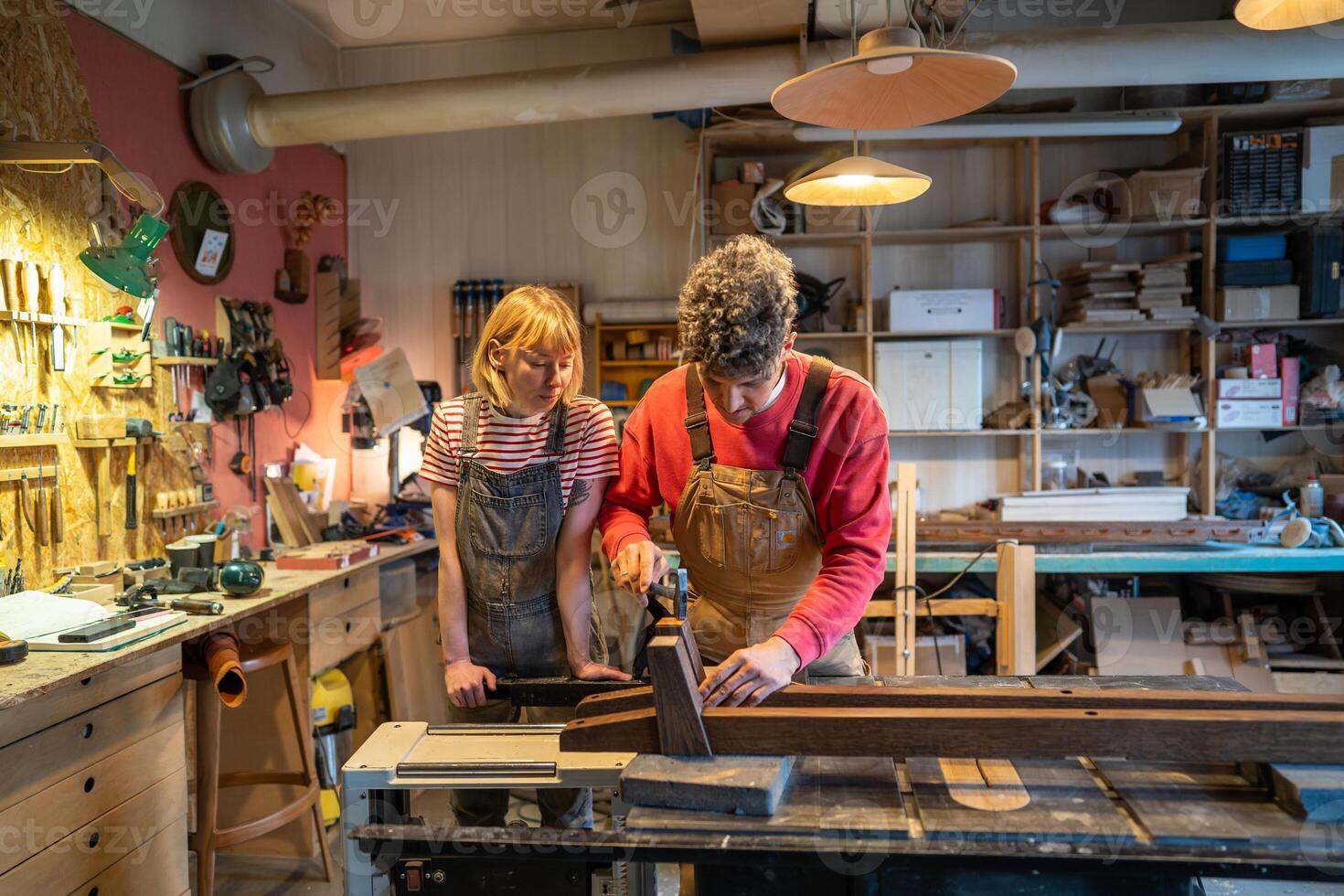 Beginner woman watch master carpenter operate saw machine in workshop. Husband and wife collaborate photo
