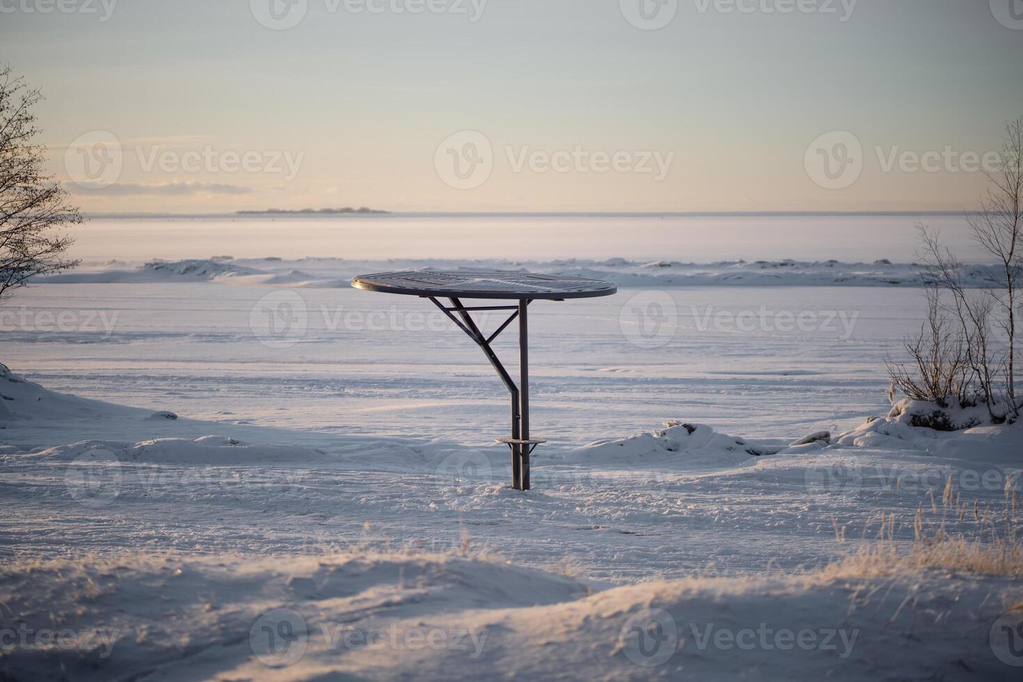 Snowy metal parasols dot empty shoreline with dramatic sky during sunrise in morning. Frosted beach photo