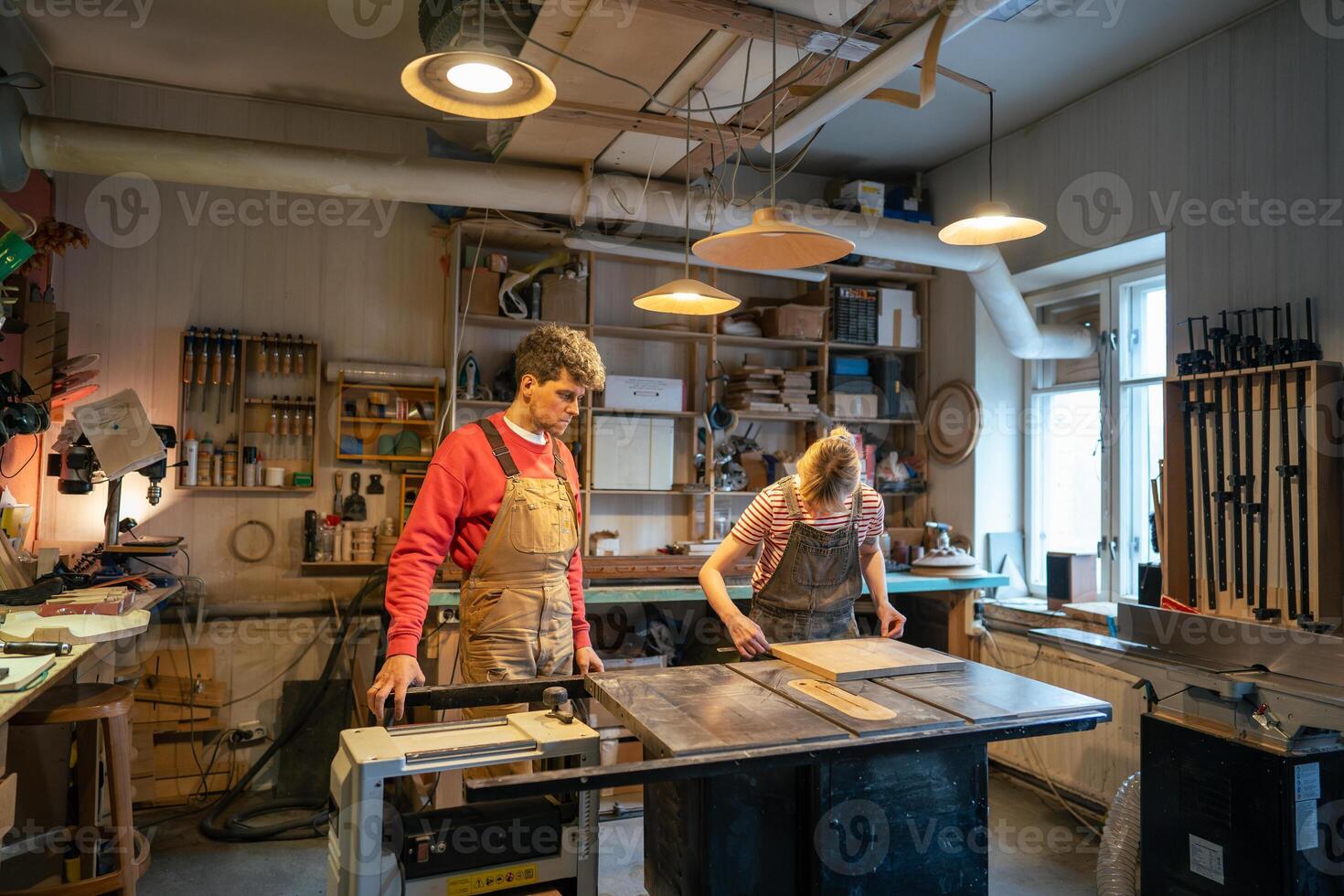 Carpenter man supervising novice woman working on circular saw table in woodworking workshop photo