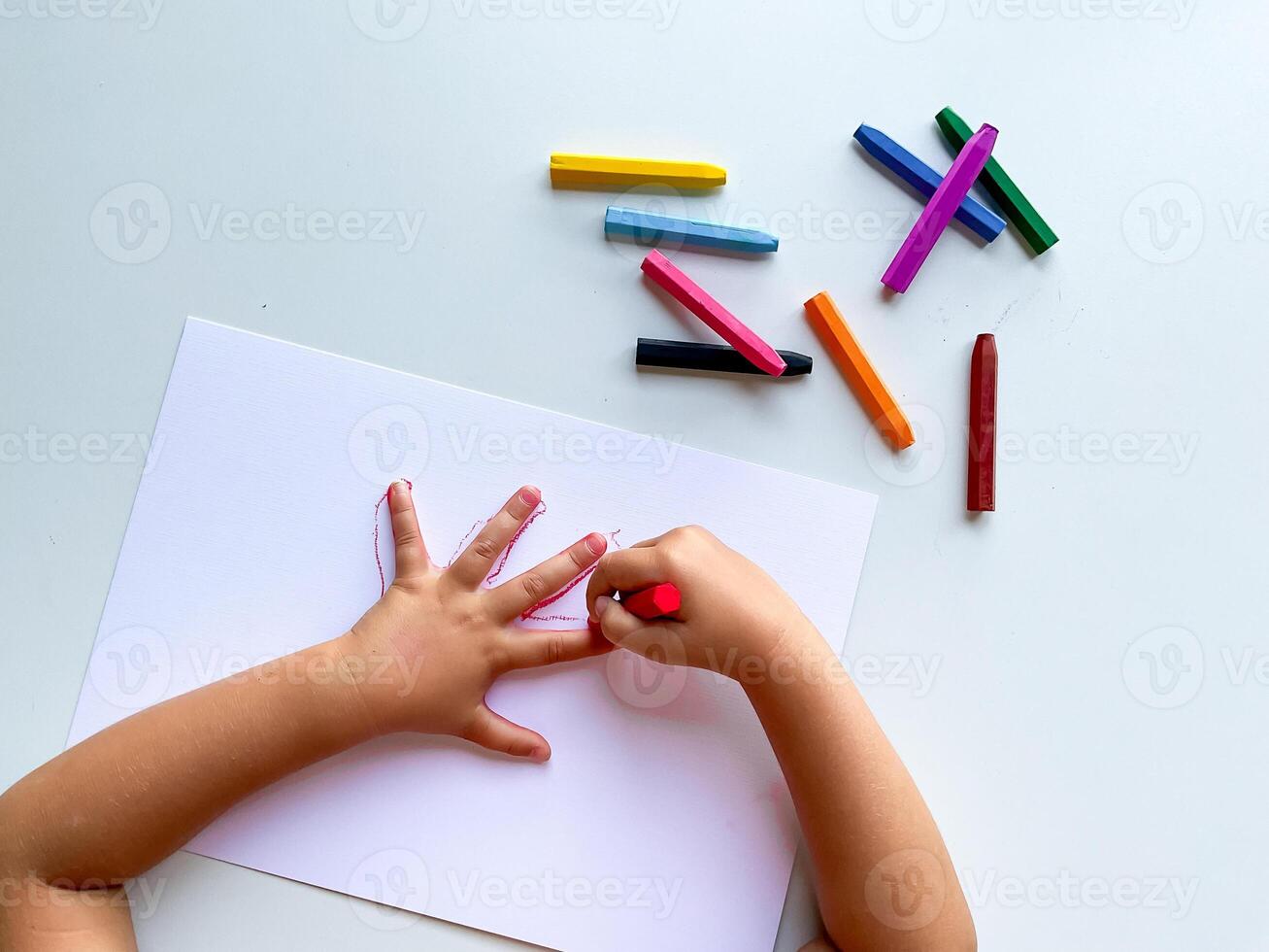 Child drawing with very colorful crayons on white paper. photo