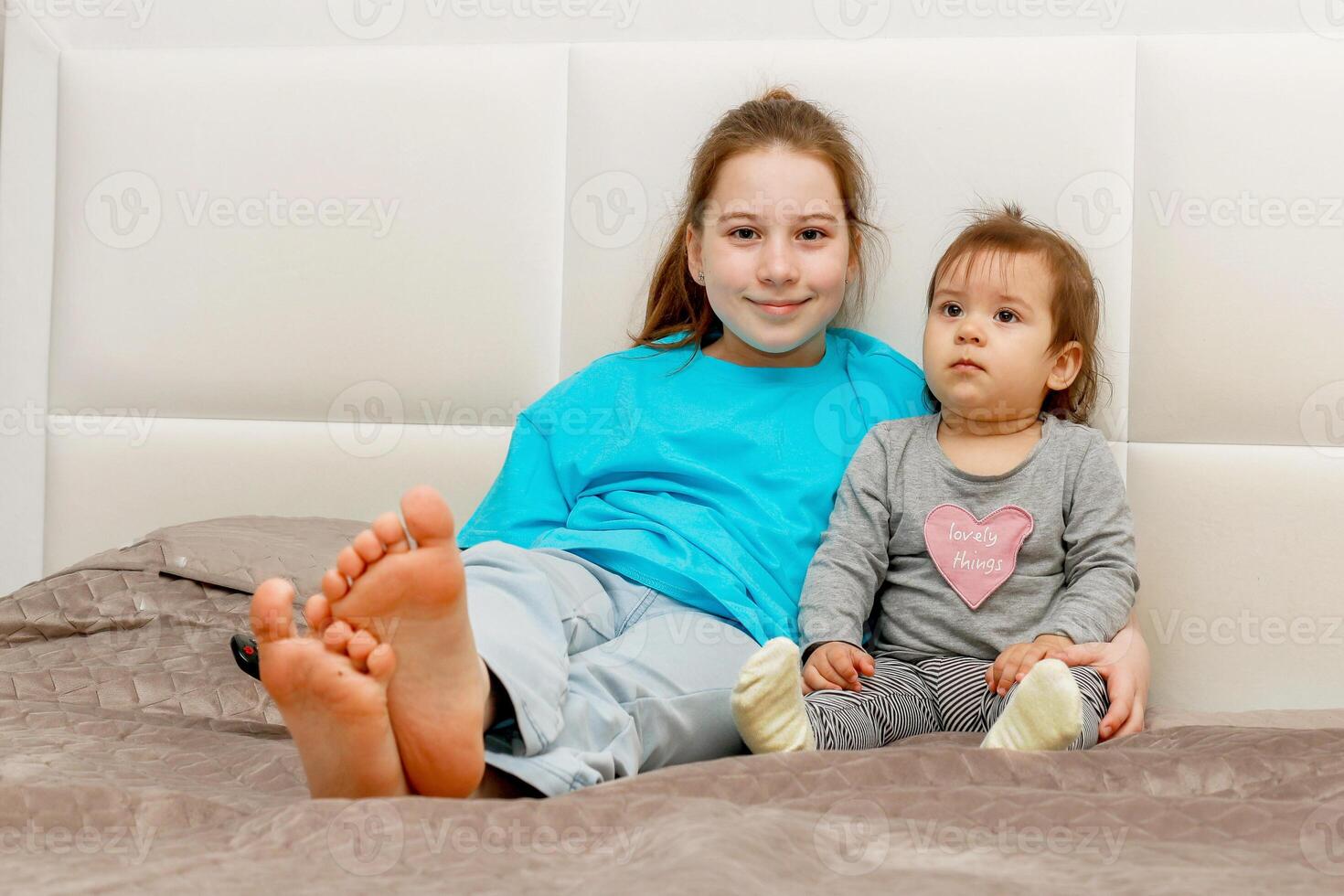 older sister hugging younger sister sitting on bed at home watching TV photo