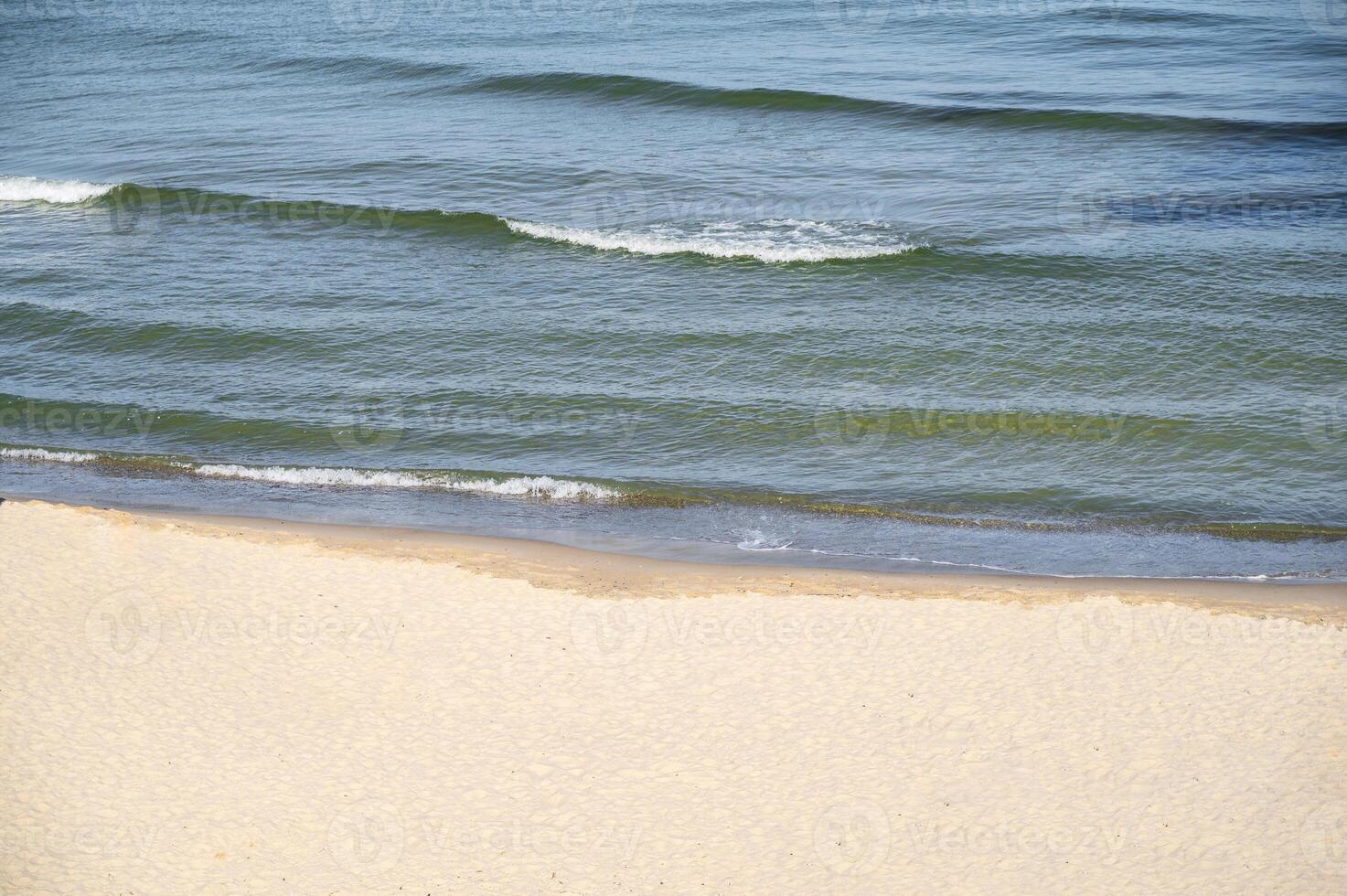 Clean sandy beach, blue sea. Calm waves roll onto the sand. Soft wave of the sea. High quality photo