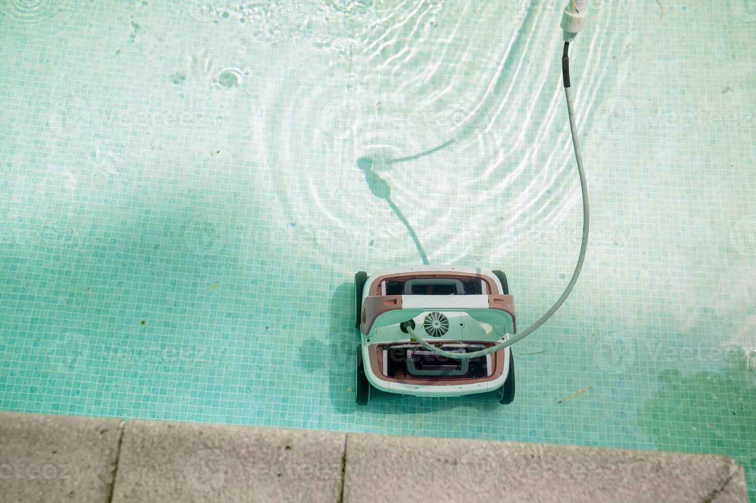 The robot pool cleaner cleans the bottom of the pool with clean water on a sunny summer day. The concept of cleaning swimming pools in hotels, resorts and country houses. High quality photo