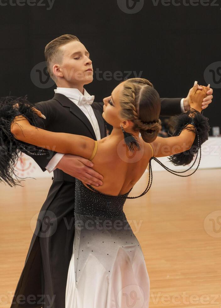 a couple dancing a standard European program on the dance floor. A young man in a tailcoat, a girl in a black and white long dress and white shoes. The couple dances a waltz photo