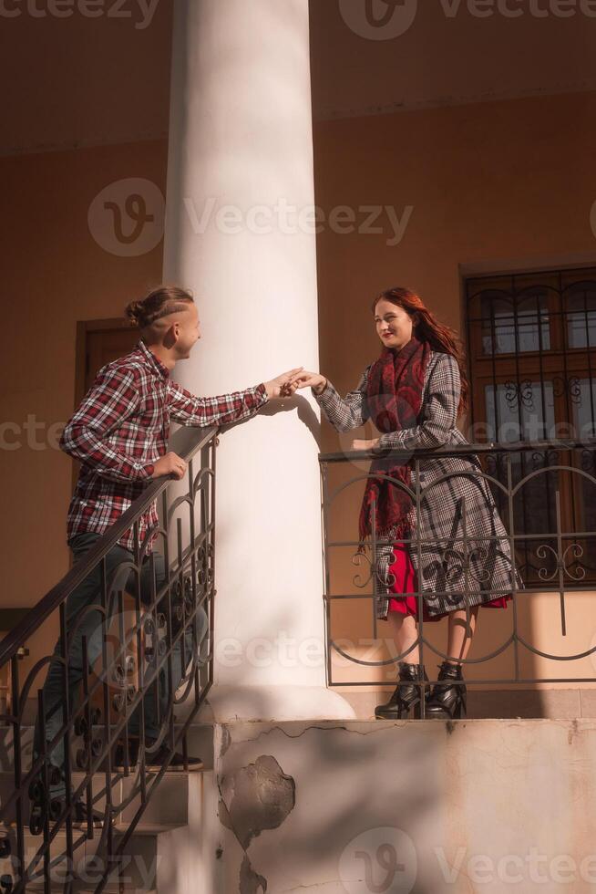 Young couple in love looking at each other romantically together. against the backdrop of an old building, in the rays of the sun. the girl is wearing a coat and a red scarf, with a hat. photo