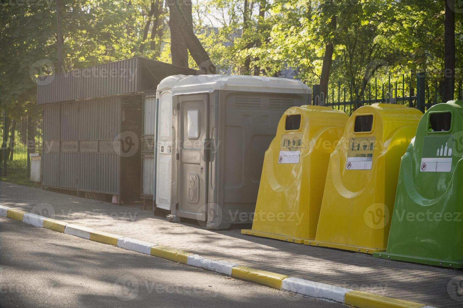 Containers for waste collection and recycling in the city park, and a bio-toilet for people with disabilities. Yellow, blue containers for recycling plastic, paper and glass waste. photo