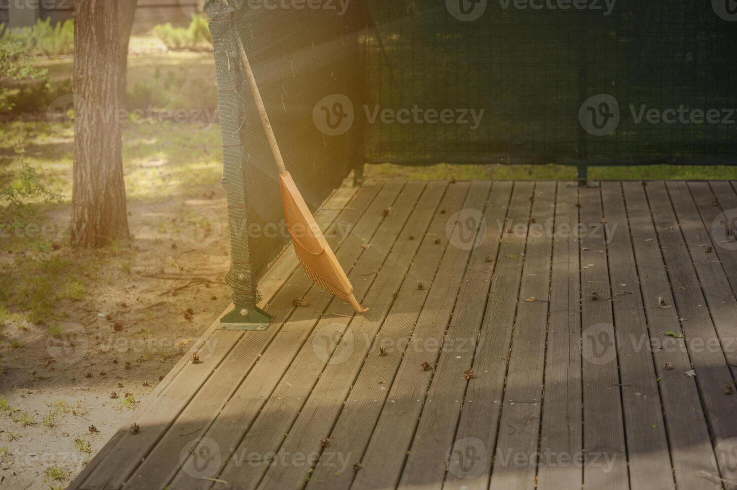 orange rake on a wooden platform, against the background of a park. pine cones lie on the wooden platform. The atmosphere is filled with sunbeams. photo