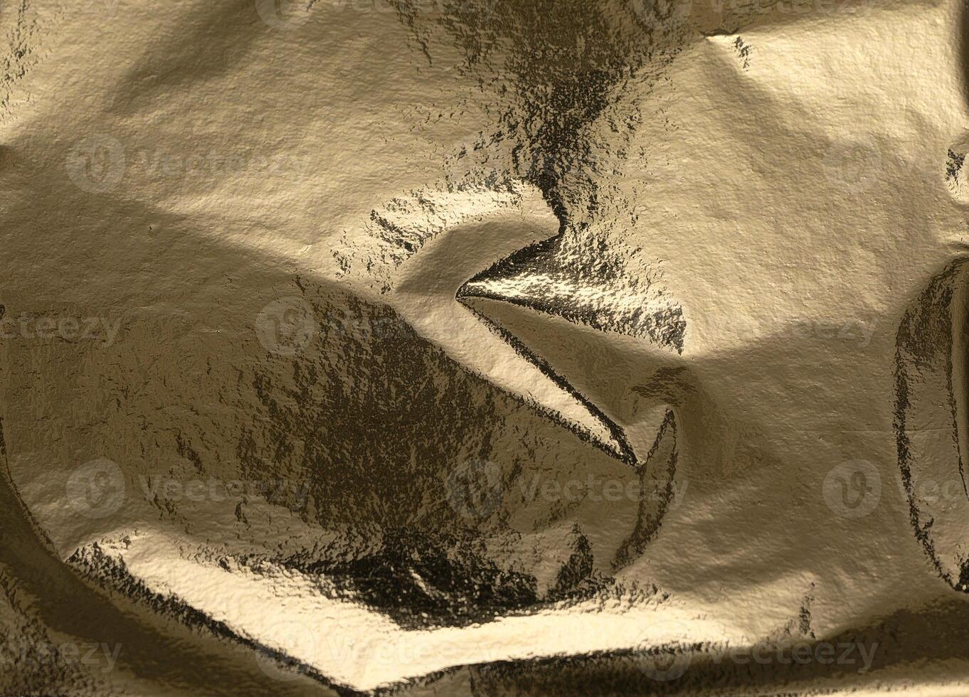 Gold foil texture with crumpled, folded metallic surface. Shiny, reflective background in rich photo