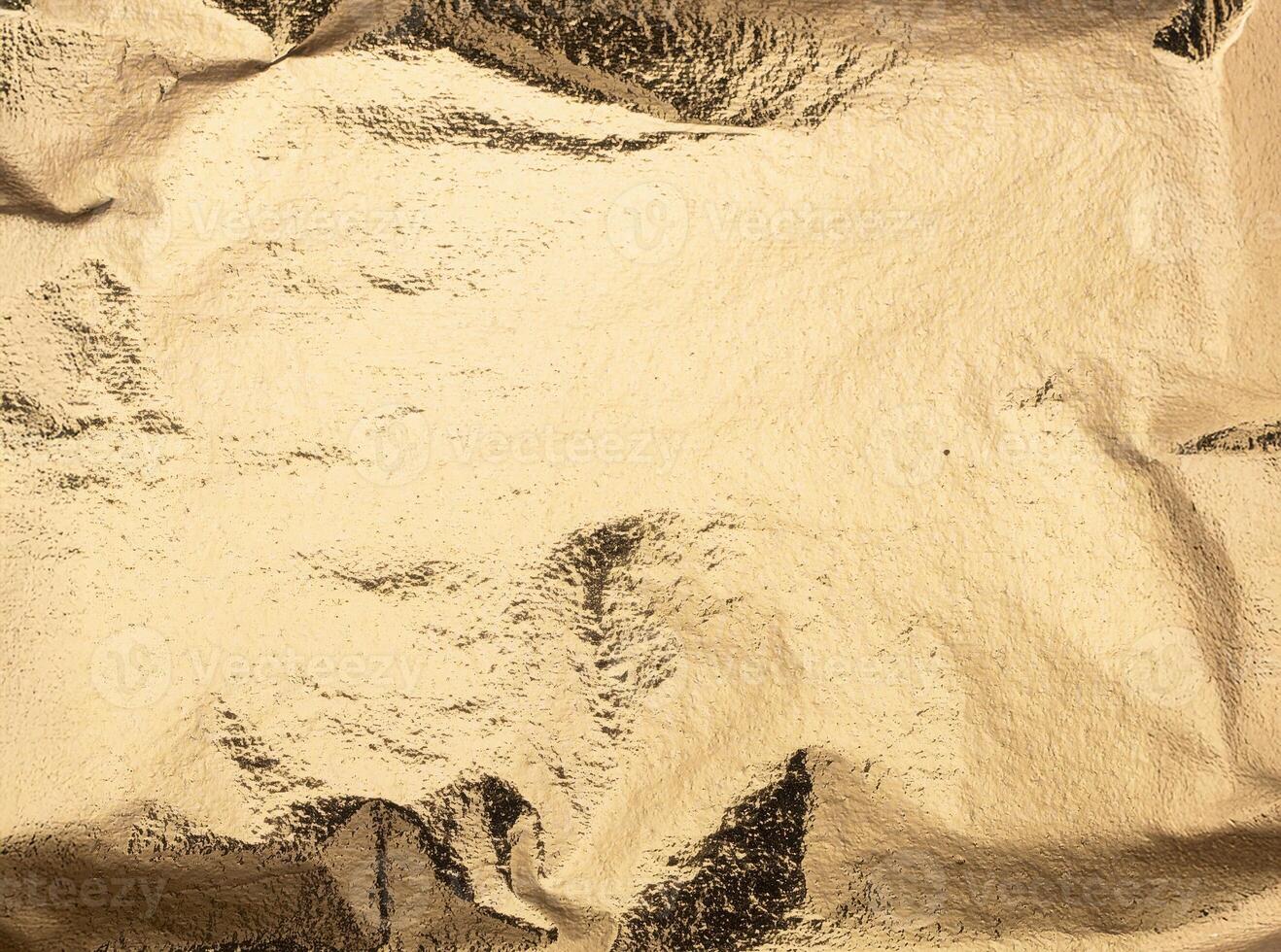 Smooth yet subtly crinkled sheet of shiny gold foil paper with reflective metallic texture, glowing photo