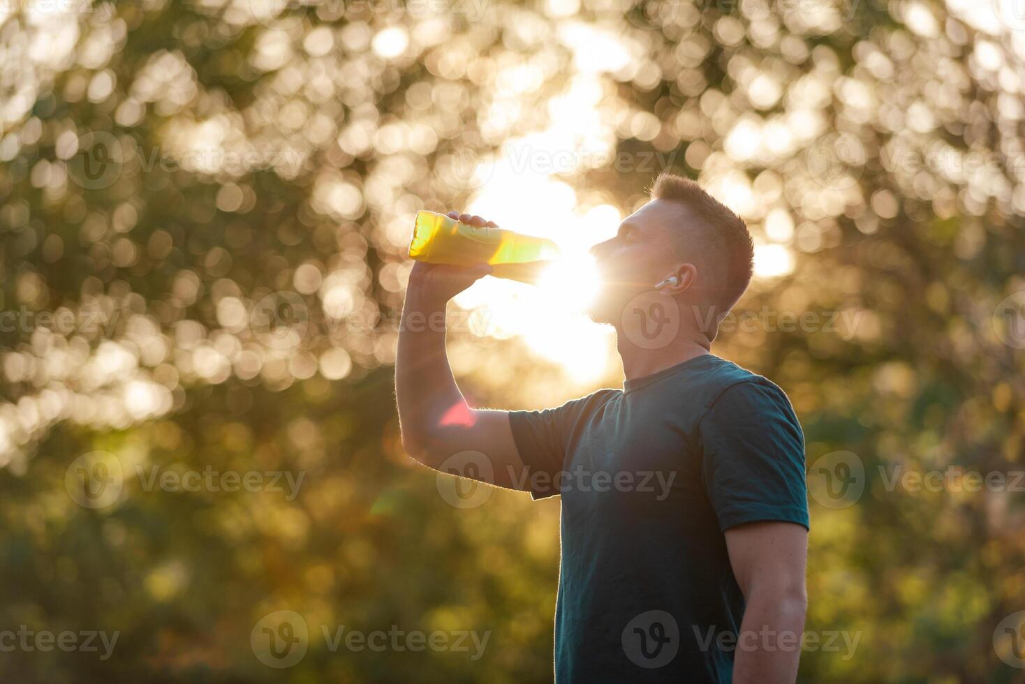A fit young man drinking water from a bottle after a run or workout in a summer park, active healthy lifestyle. photo