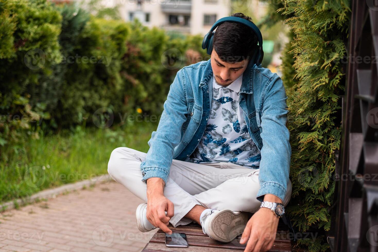 A young man with headphones using a mobile phone outside. photo