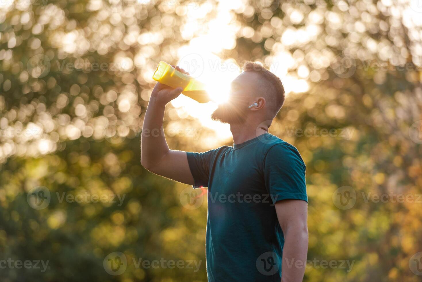 A sporty young man drinking water from a bottle after a run or workout in a summer park, active healthy lifestyle. photo
