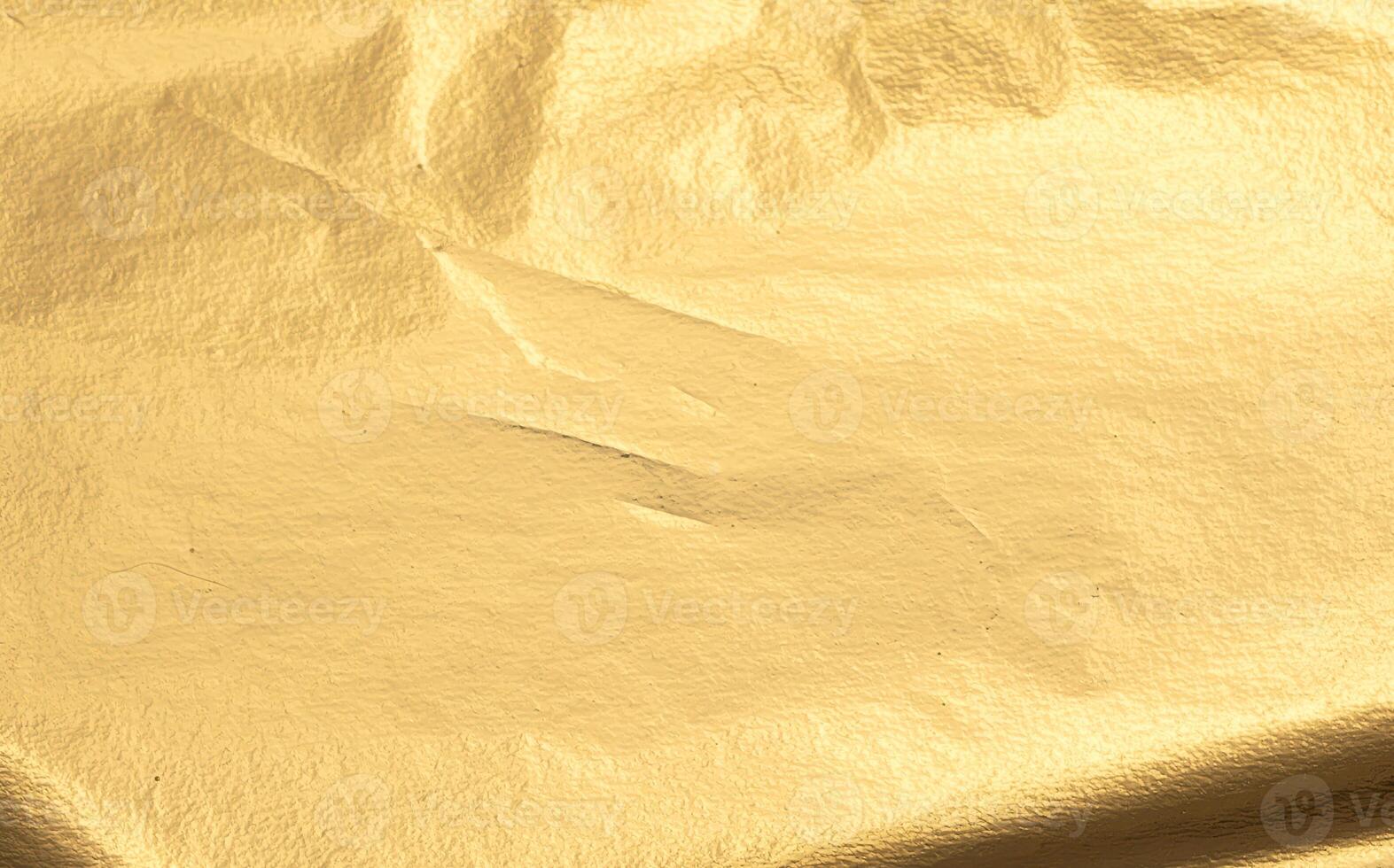Gold metallic foil texture with a smooth, creased surface. Shiny, reflective material in warm yellow photo