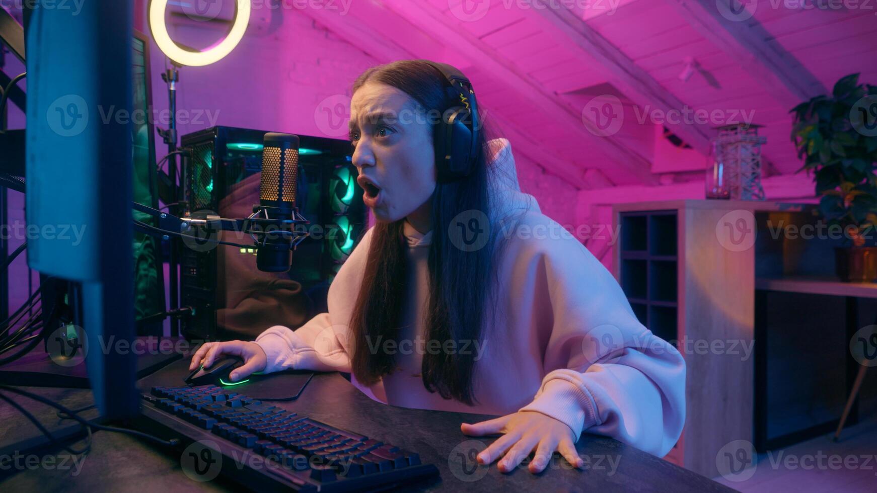 Angry upset young woman girl female streamer gamer in headphones sitting at desk with keyboard computer monitor emotional playing online game loss shouting frustrated intense reaction in neon room photo