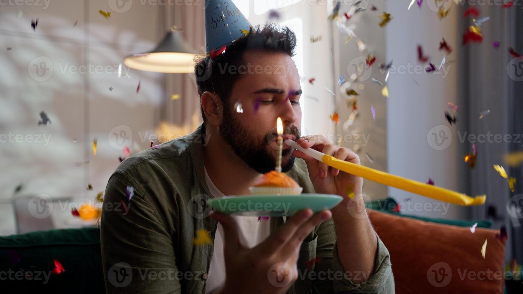 Upset unhappy depressed Caucasian man male homeowner lonely celebrating birthday in festive hat blowing whistle holding cake muffin confetti falling depression mental health problem loneliness at home photo