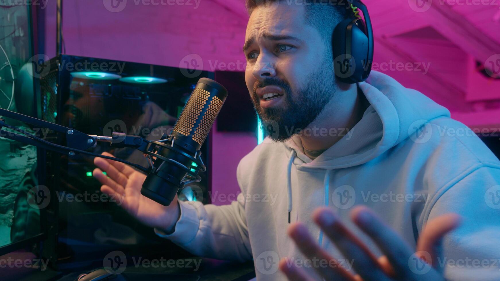 Caucasian guy male gamer streamer man playing online game lose upset bad result disappointed suffer failure end gaming loser in headphones talking in microphone streaming in neon dark room at home photo