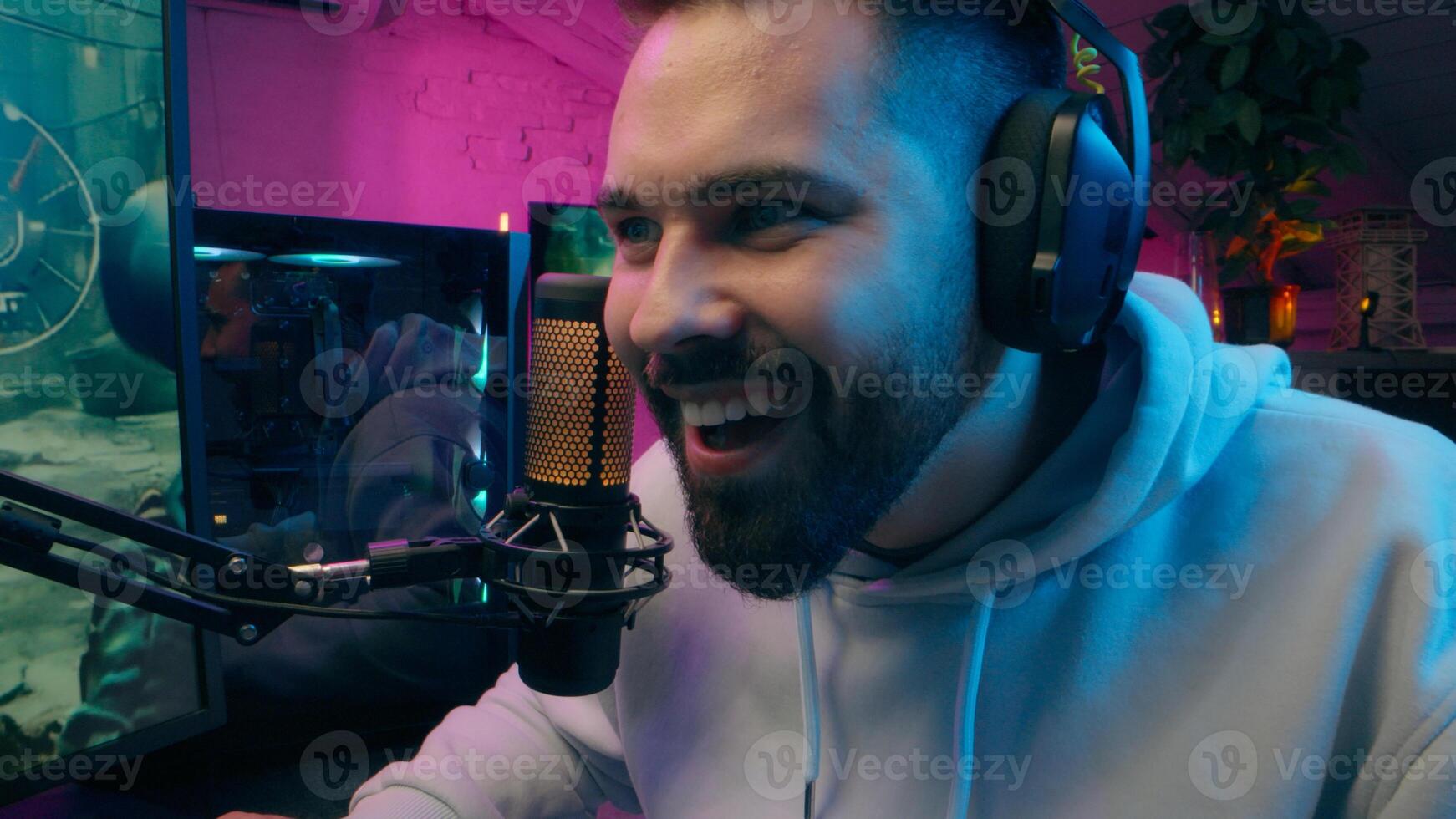 Positive emotional Caucasian guy gamer man streaming addiction streamer playing computer game cyber sport at home night Internet influencer smile blogger male recording gaming blog e-sport neon photo