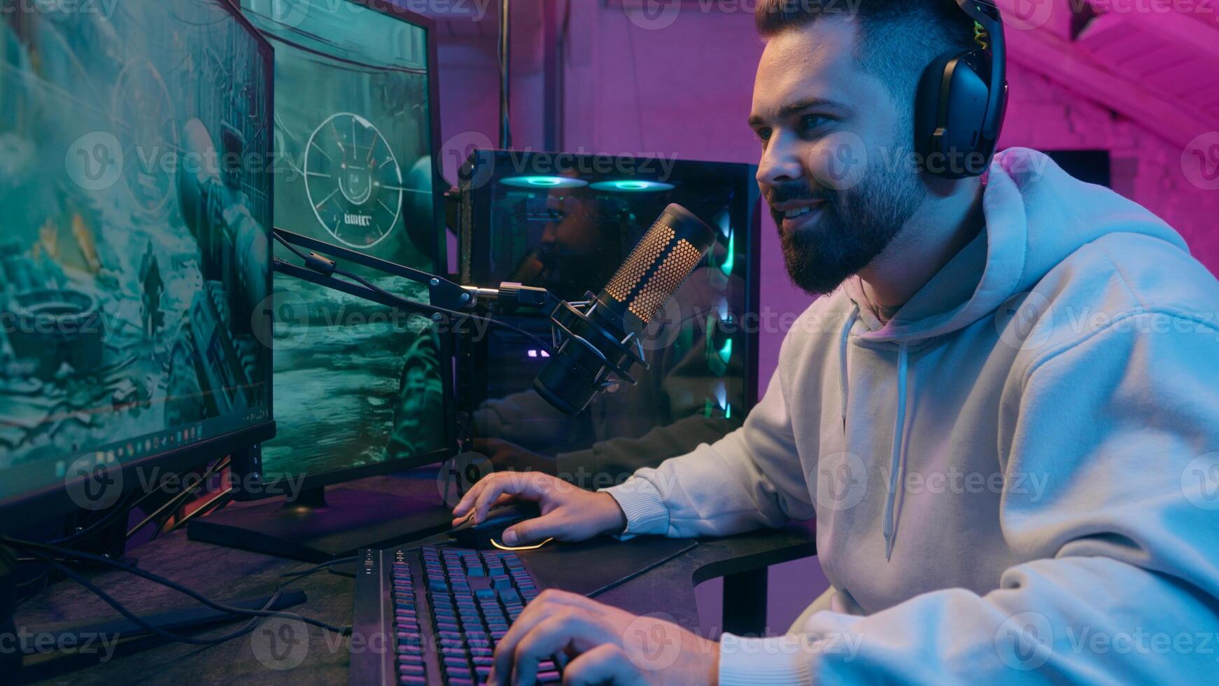 Addicted Caucasian guy male gamer streamer man play online battle enjoying smiling wearing headphones gaming at computer streaming in neon dark room at home match digital playing looking internet game photo