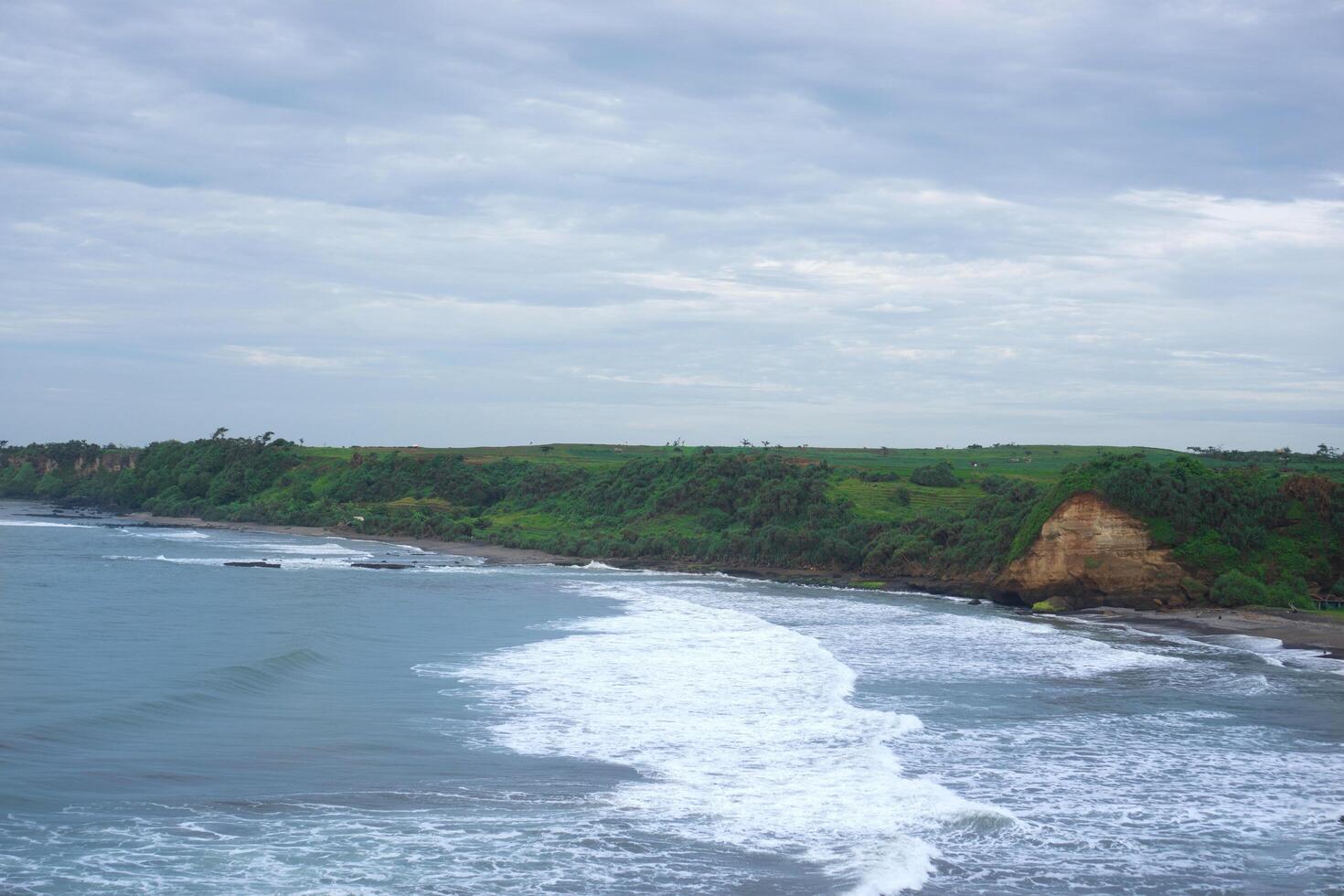panorama of the scenic view of the beach from a green cliff with very large sea waves. at santolo beach, west java, indonesia photo