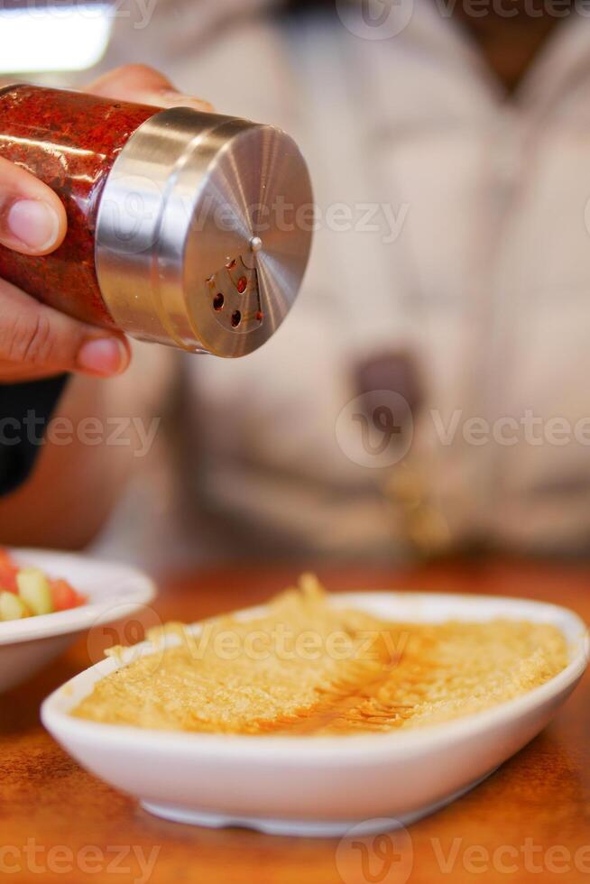 Person adding spice to food at a dining table photo