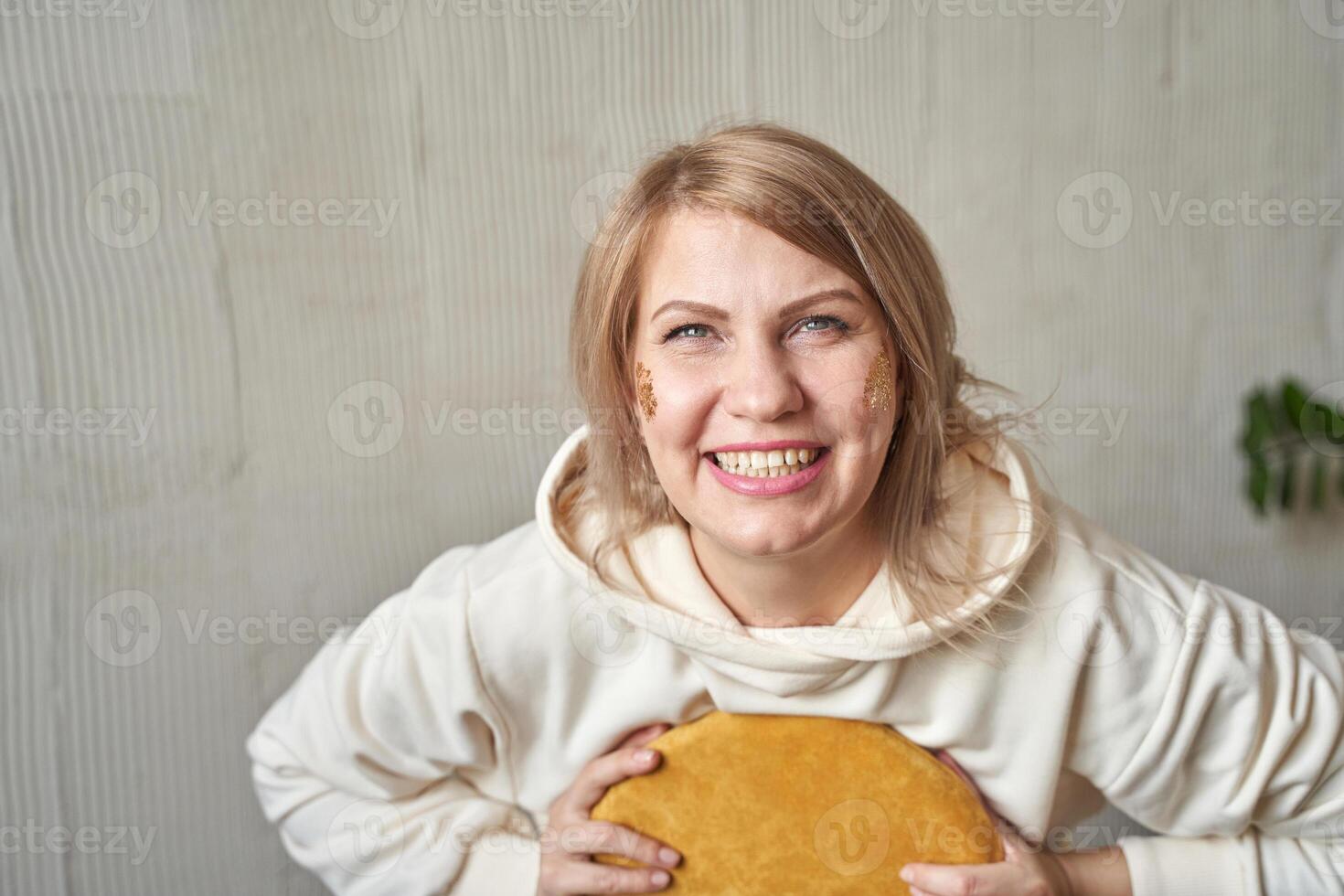 Caucasian young adult female smiling holding round pillow against textured wall. photo