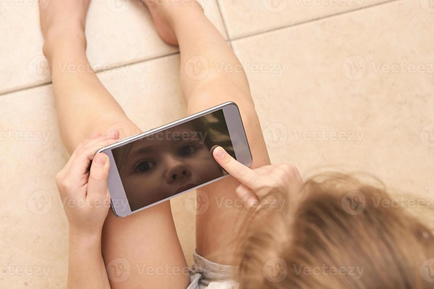 Young caucasian child engaged with smartphone technology reflection on screen. photo