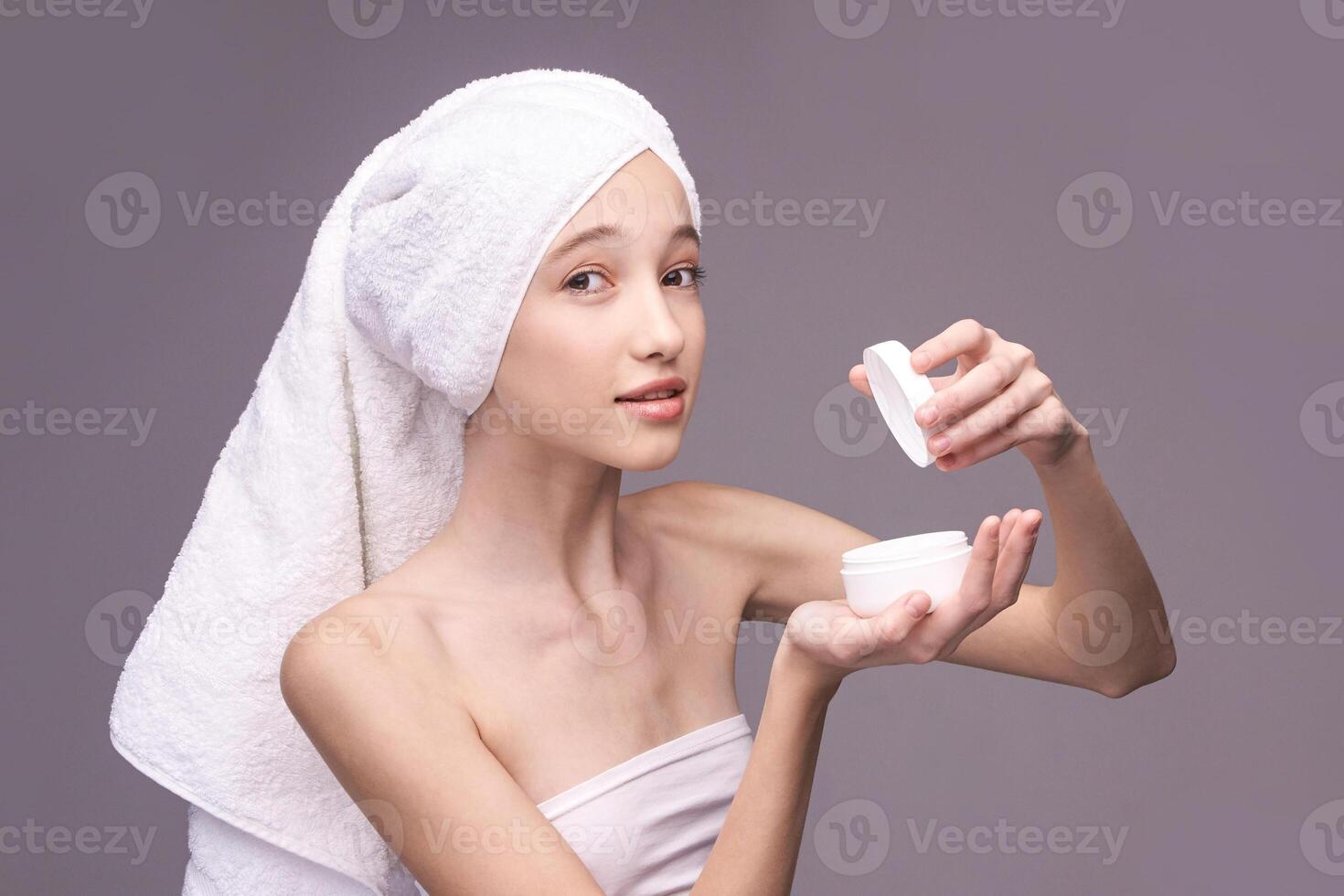 Young caucasian female applying skincare cream with towel on head in relaxed setting. photo