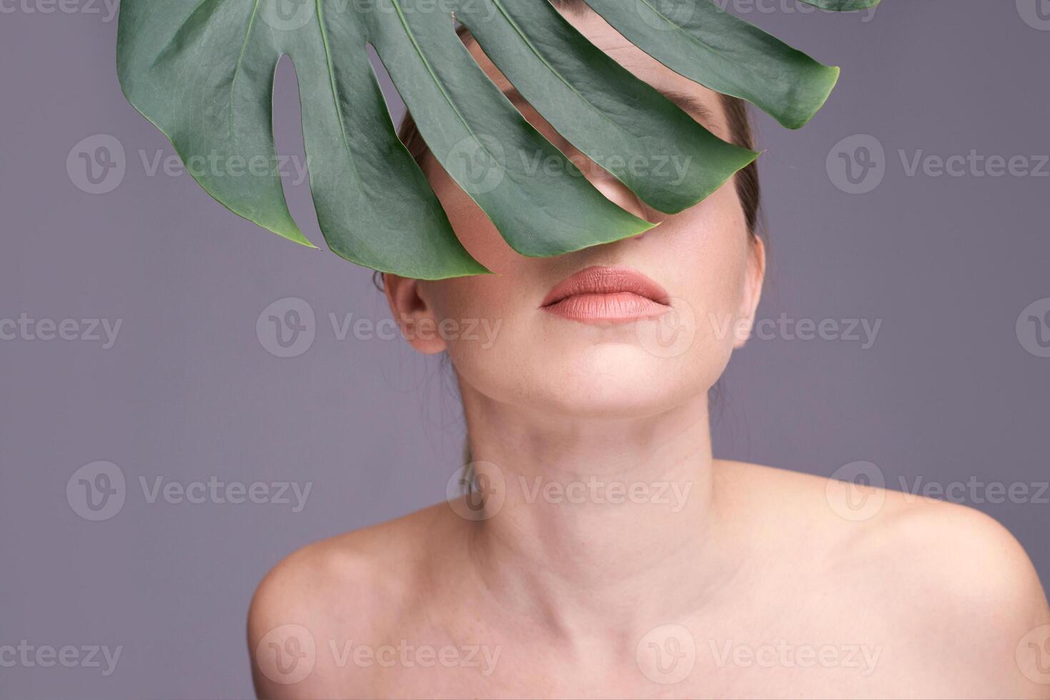 Young caucasian female partially covered by monstera leaf with neutral expression in studio setting. photo