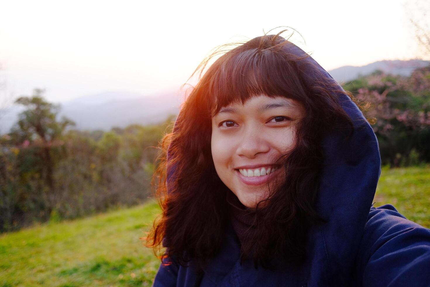 Traveler Asian woman wearing jacket and hood smiling on blue sky with sunrise in winter on the hill with valley Doi Luang Chiang Dao mountain view, Chiangmai of Thailand photo