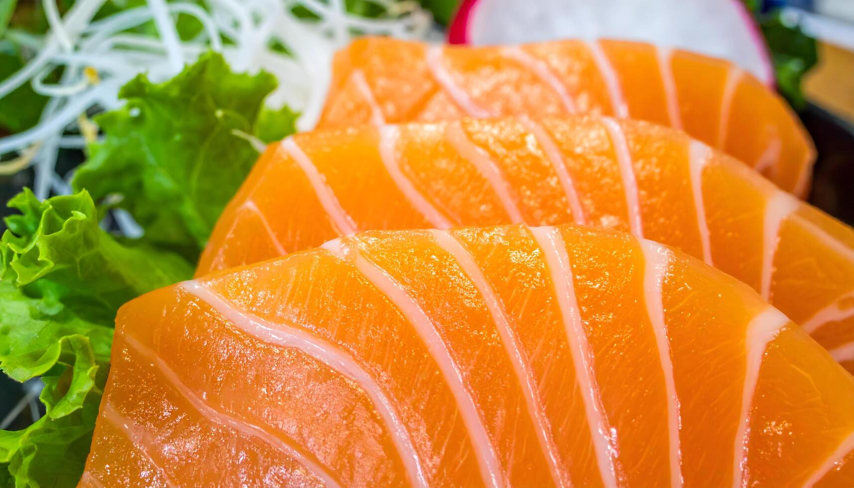 Slices of fresh salmon sashimi arranged on a black plate with garnish. Rich orange color and fine marbling highlight Japanese cuisine. Perfect for sushi, culinary, and food photography themes. photo