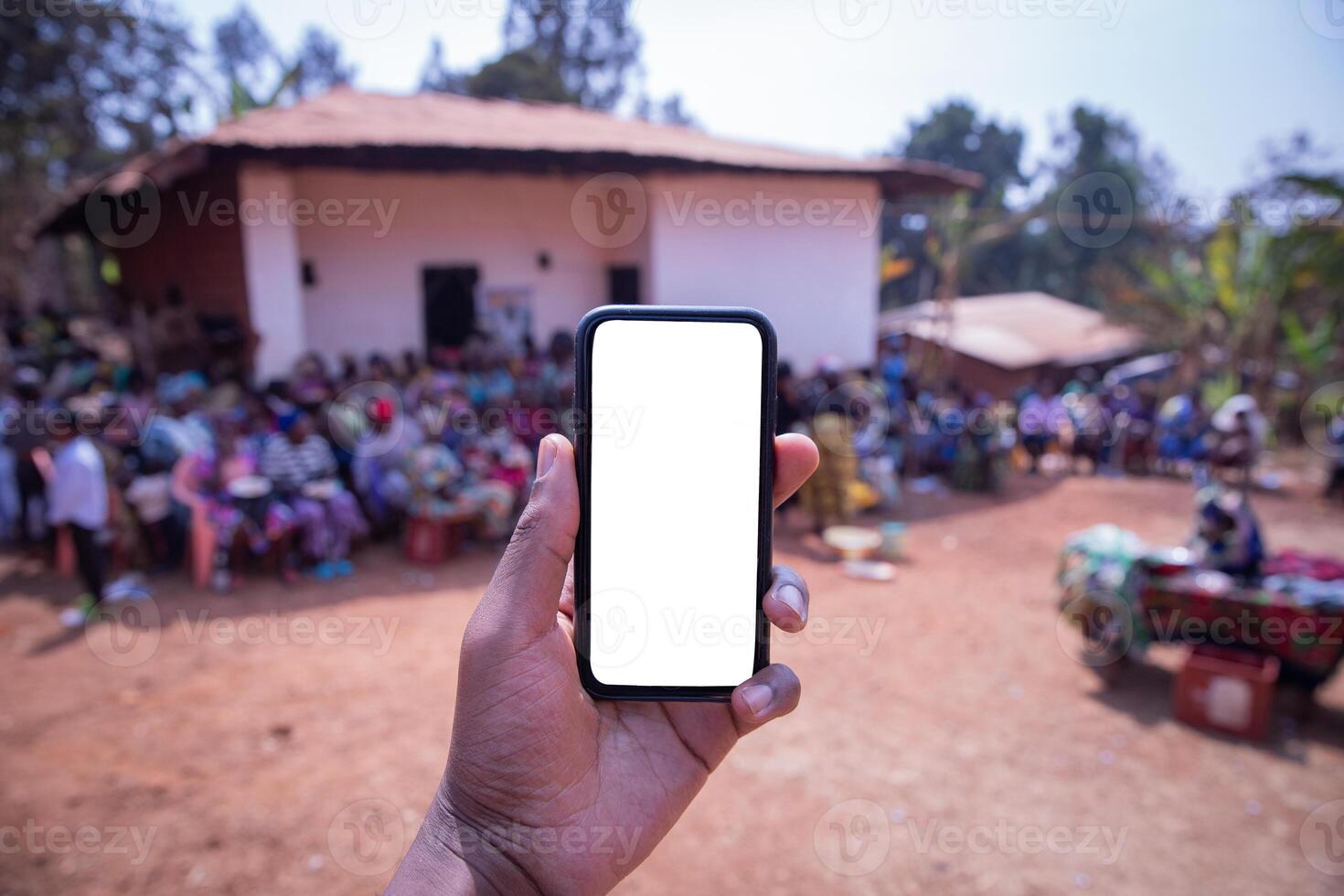 Mock up of the screen of a smartphone held by a hand with an African village in the background with people sat photo