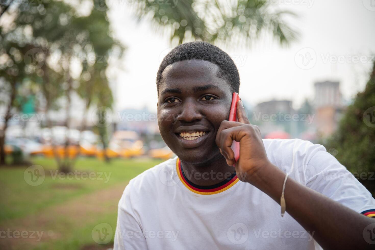Portrait of an African boy making a phone call with his smartphone while outdoors in a public park. photo