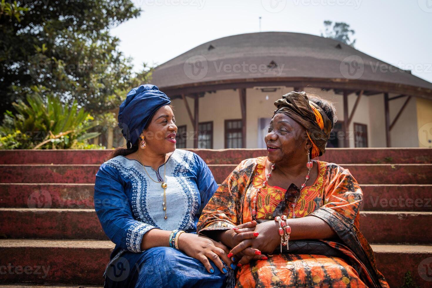 Two African women are conversing sitting on the stairs, they are both dressed in traditional clothes photo