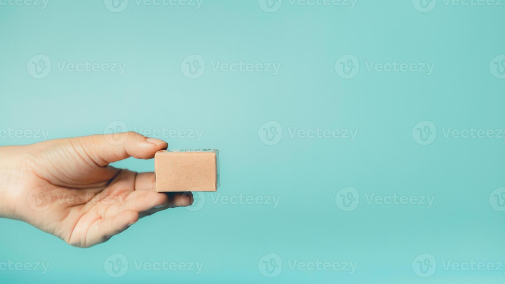 Female hand holding a mini wooden parcel box on blue background. Copy space. photo