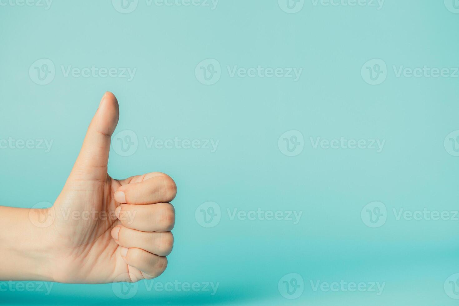 Female hand showing thumbs up sign on blue background with copy space. photo