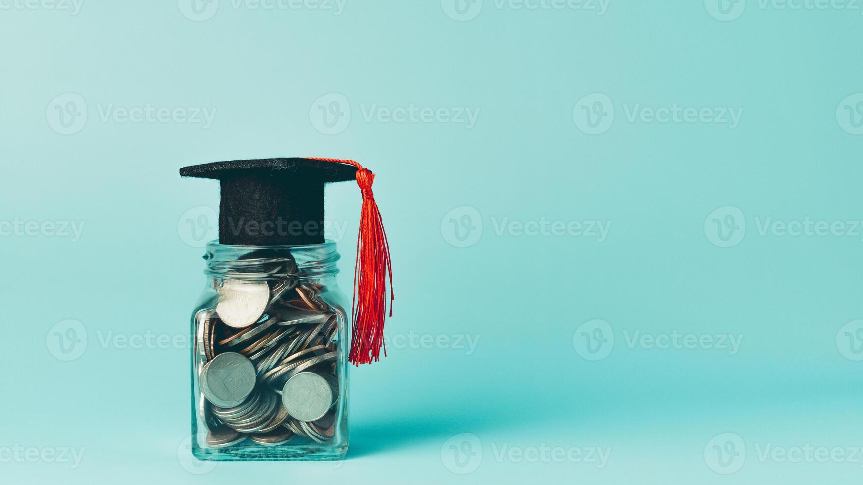 Coins in a glass jar with a graduation cap on a blue background. photo