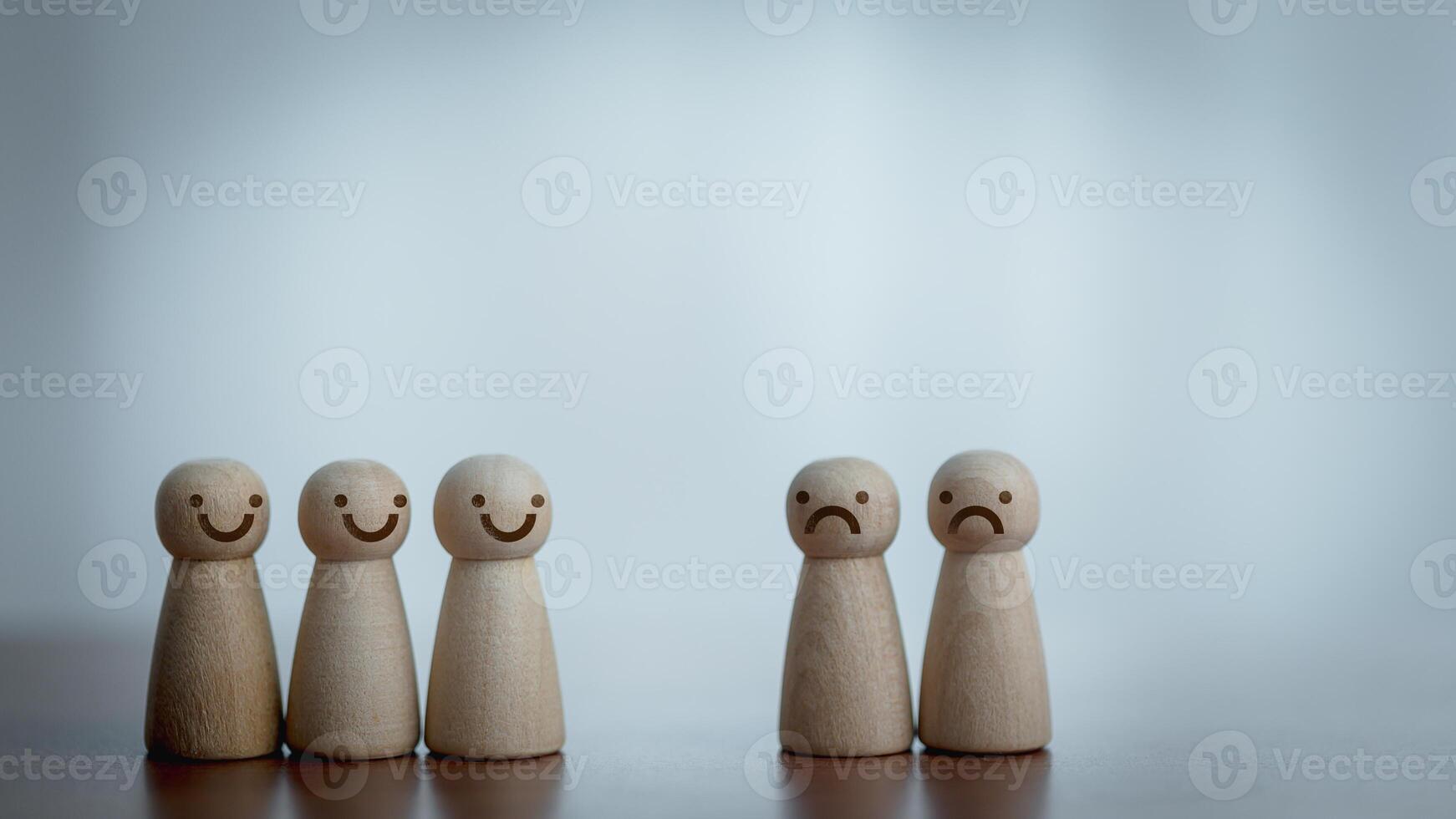 Two Groups of Wooden Figurines Showing Joy and Sadness on a Wooden Table with Blurred Background photo