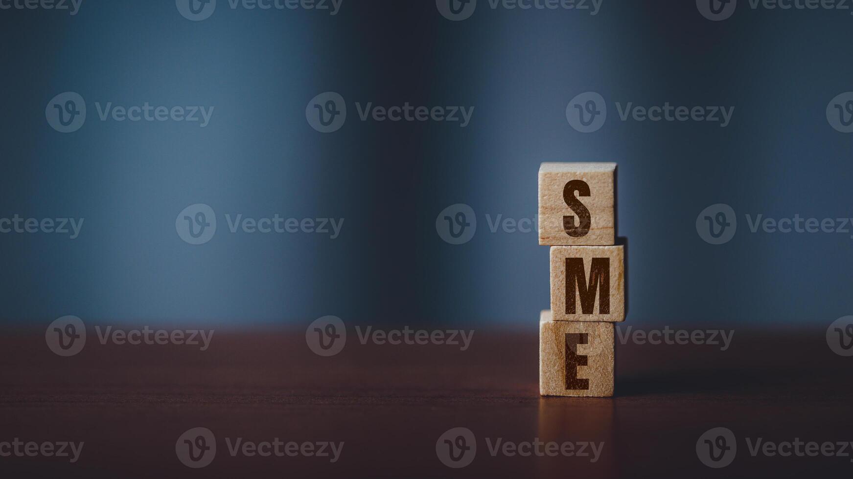 Stacked Wooden Cubes Spelling SME on a Dark Toned Table with Blurred Background photo