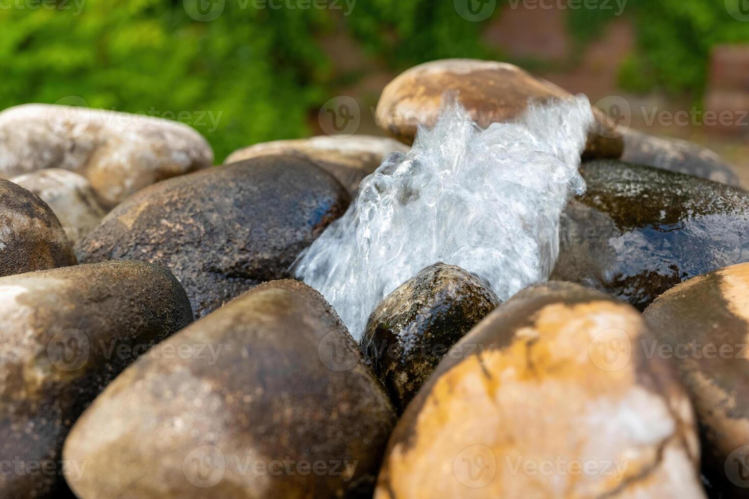 Glistening water cascades over smooth stones in a tranquil garden setting on a sunny day photo