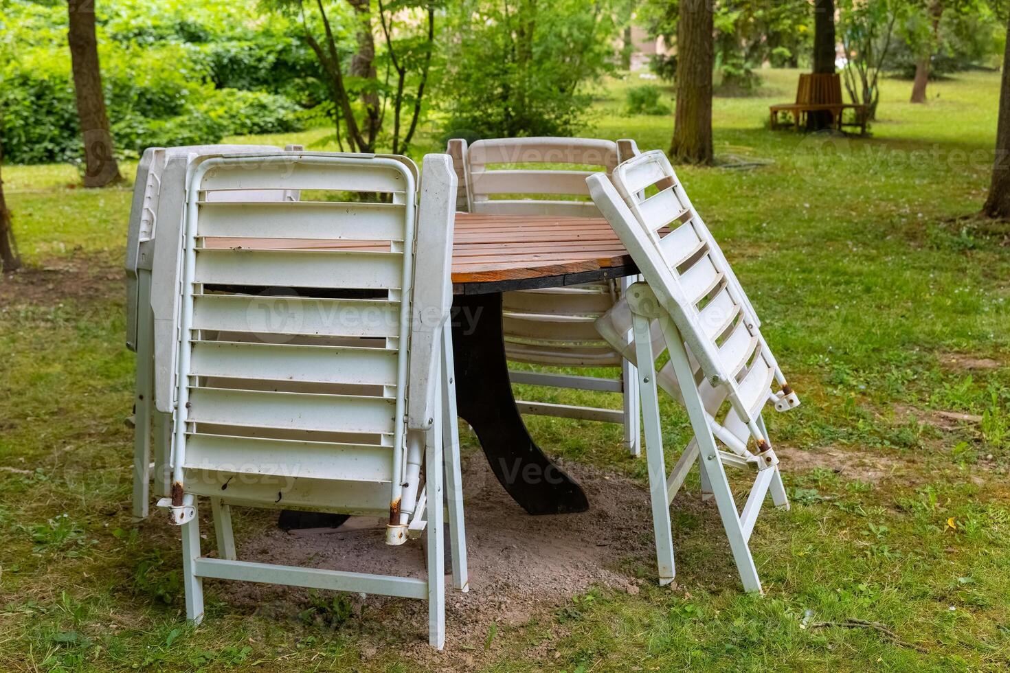 Empty outdoor dining area with stacked chairs against a wooden table surrounded by green scenery in a park photo
