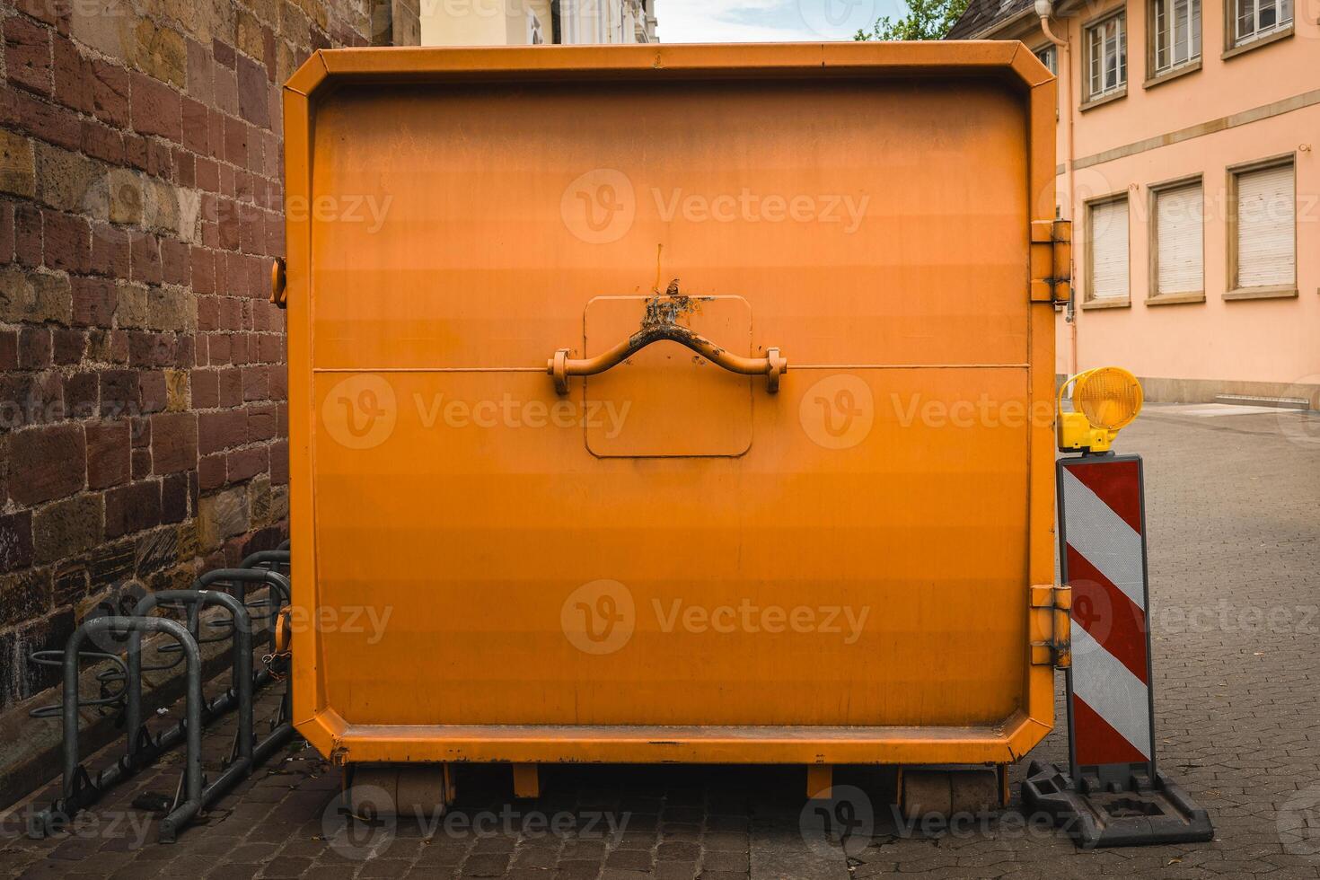 Bright orange dumpster standing out against the rustic architecture in a quiet European street during the day photo