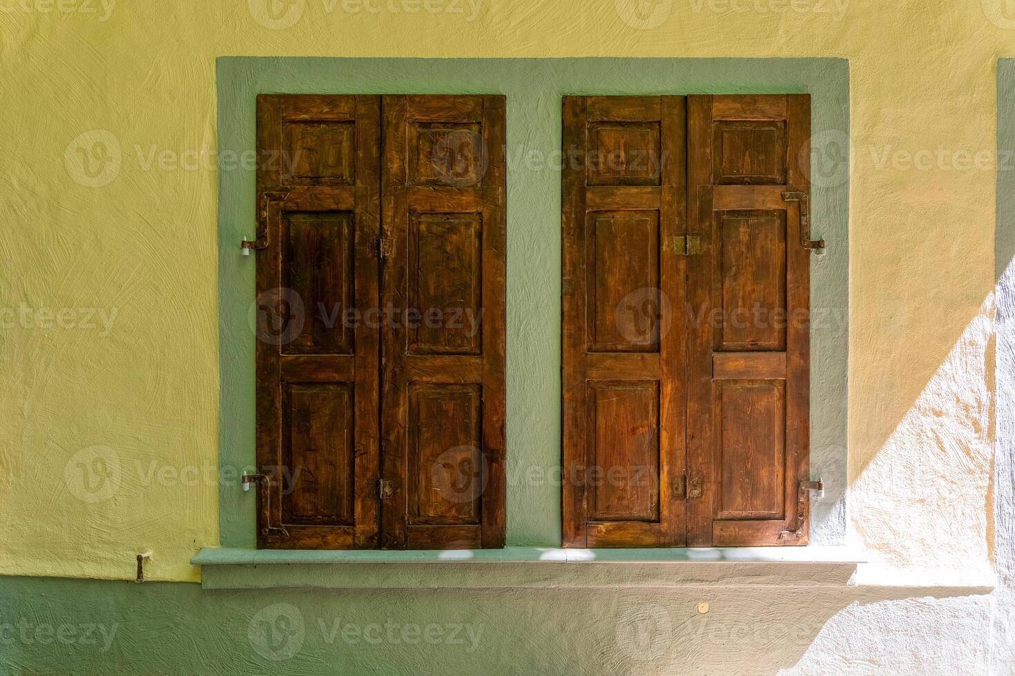 Intricate wooden shutters grace a charming yellow wall capturing the essence of rustic architecture in a serene setting photo