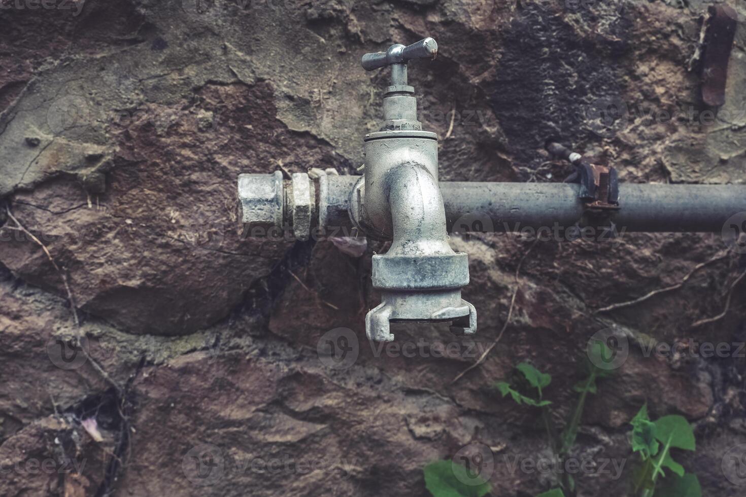 Water faucet emerges from rocky wall showcasing rustic charm in a forgotten outdoor space at twilight photo