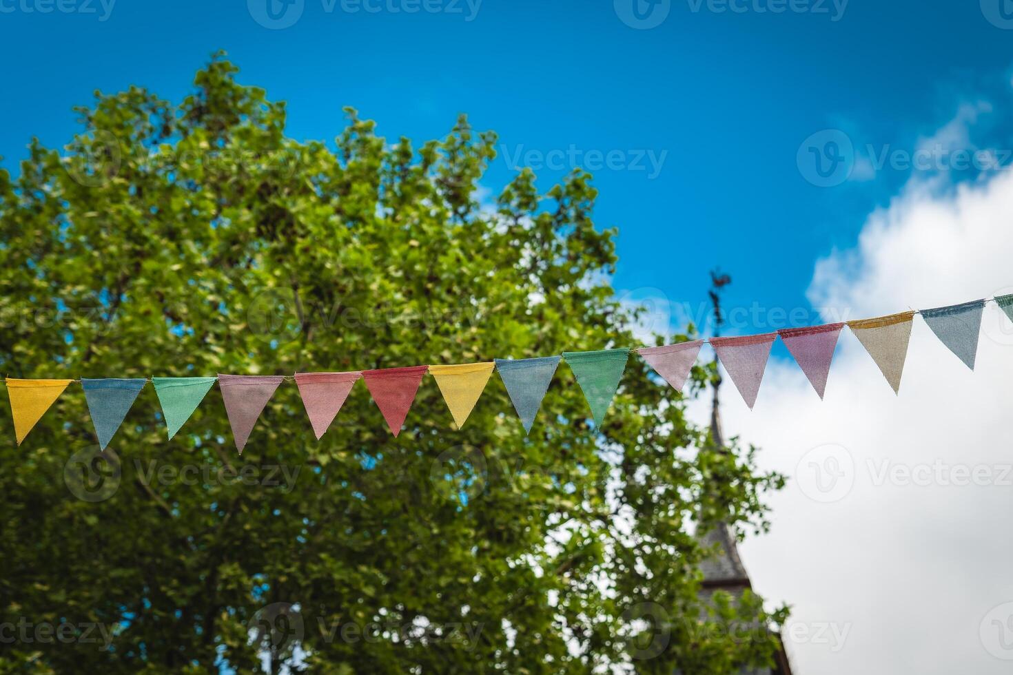 Colorful bunting flutters under a blue sky at a lively outdoor gathering in a park photo